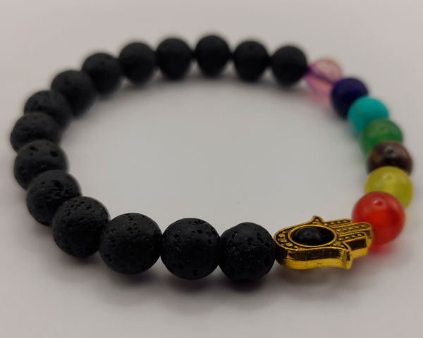 Pulsera de piedra volcánica con cuentas de chakra en colores vivos y un colgante de Hamsa dorado con un ojo central, representando protección y equilibrio espiritual.